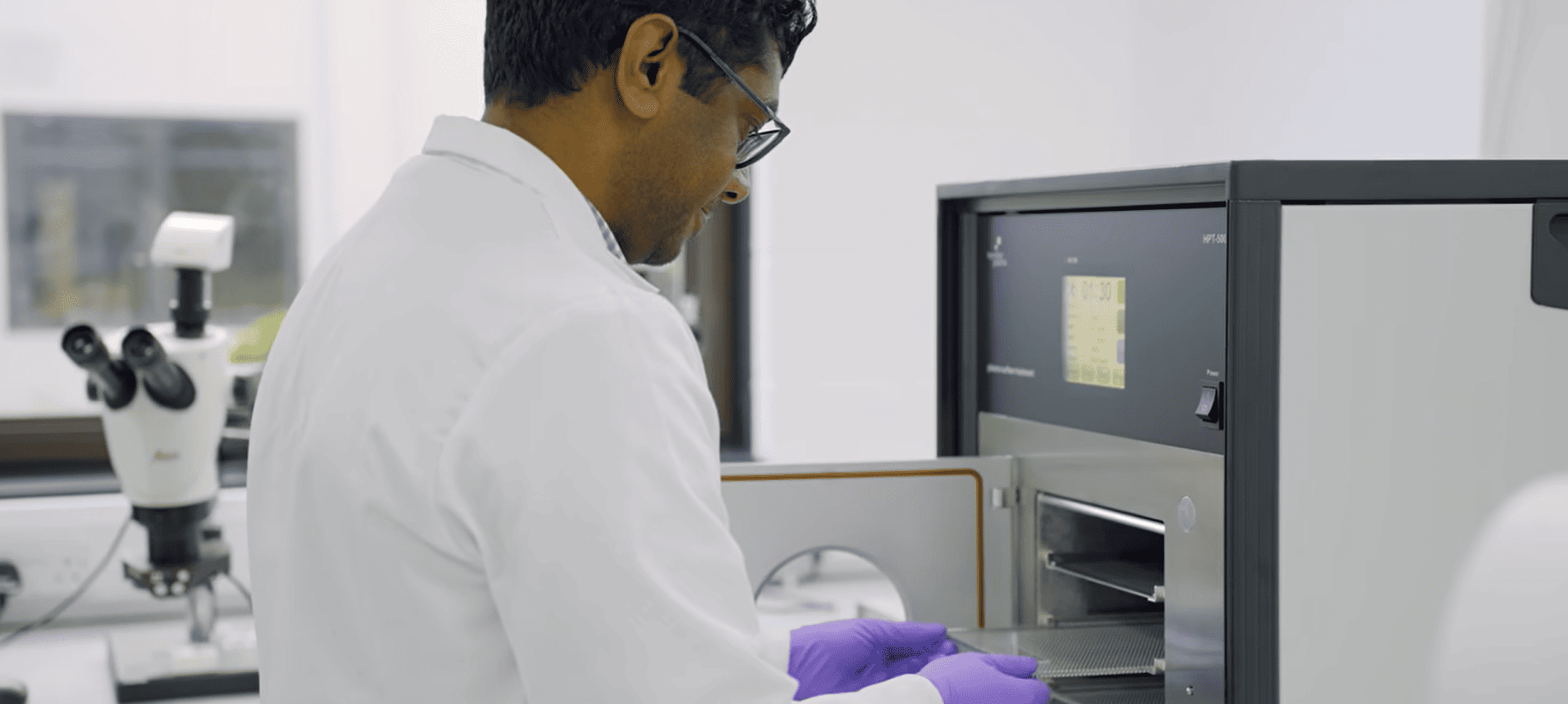 Scientist loading plasma treatment chamber for medical device surface activation in clean lab environment